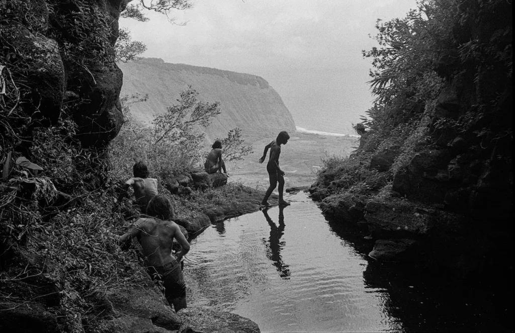 Photo of shirtless Hawaiian kids crossing a stream hiking Hiilawe