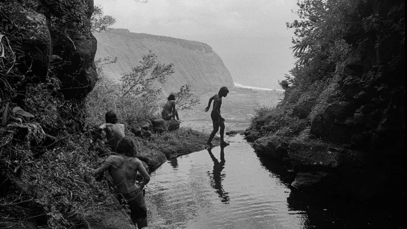 Photo of shirtless Hawaiian kids crossing a stream hiking Hiilawe